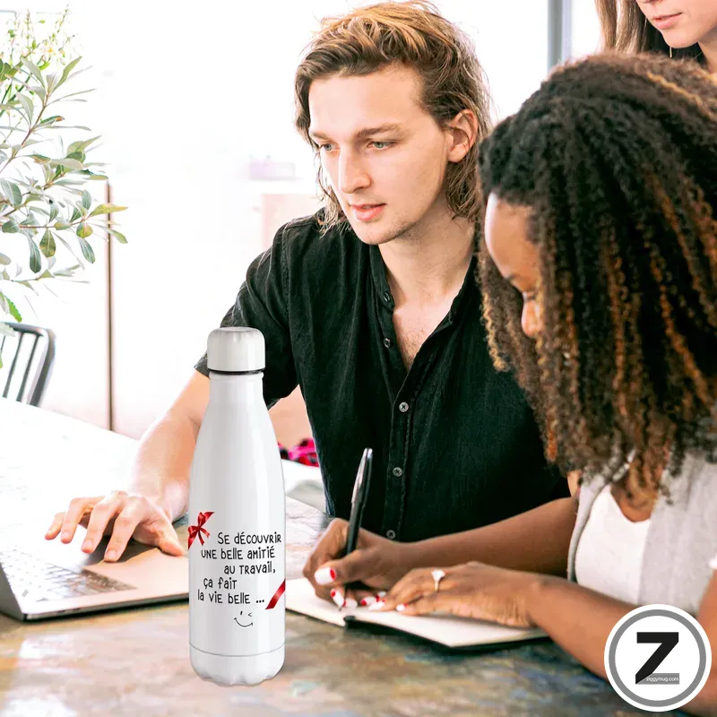 Two people collaborating at a table; a white insulated bottle with French text sits near a laptop and notebook in the foreground.