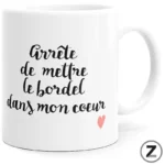 White ceramic mug with black cursive French text 'Arrête de mettre le bordel dans mon cœur' and a small pink heart.