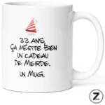 White mug with a small party hat and French text that reads: '33 ans ça mérite bien un cadeau de merde. Un mug.'