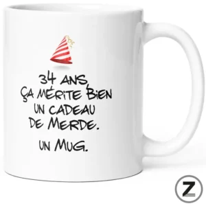 White ceramic mug featuring a handwritten-style French joke about turning 34, with a small party hat illustration above the text.