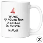 White mug with black handwritten French text joking that 36 years deserves a 'shitty gift'—a novelty mug., with a small red party hat illustration on the left.