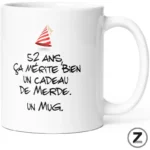 White mug with a red party hat and a humorous French phrase about turning 52: '52 ans, ça mérite bien un cadeau de merde. Un mug.'