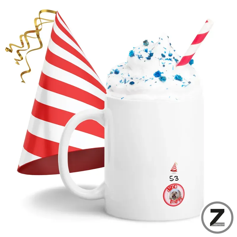 White mug topped with whipped cream and blue sprinkles, with a red-and-white striped straw and a striped party hat nearby for a festive look, plus curling ribbons and a small round logo on the mug.