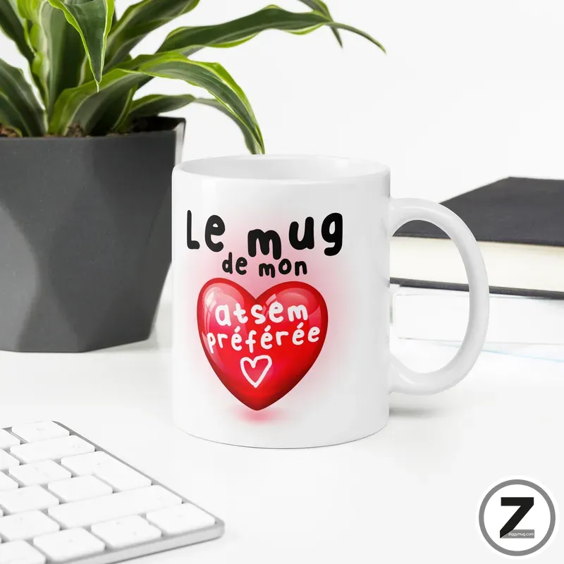 White ceramic mug with a red heart and French text on a clean desk near a plant.