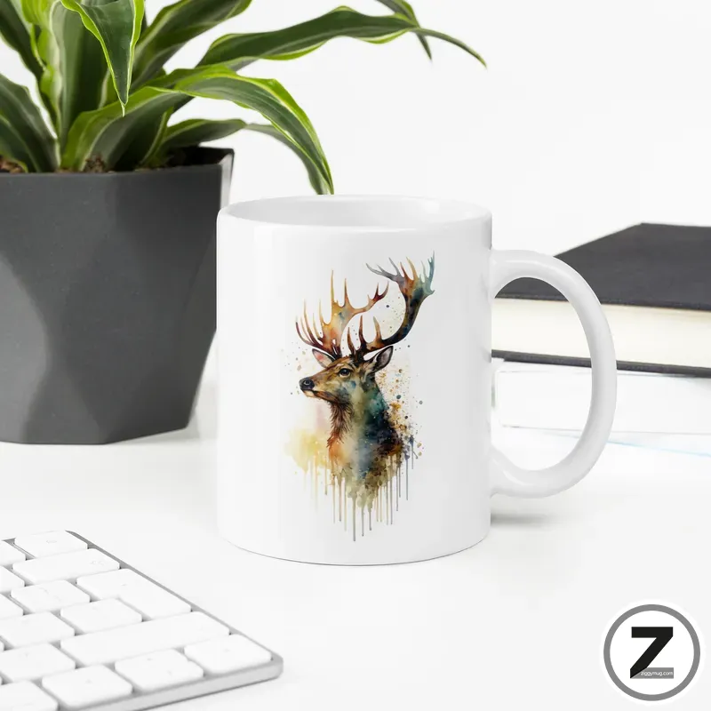 White ceramic mug featuring a watercolor-styled stag illustration with splashes and drips of color on a desk setup.