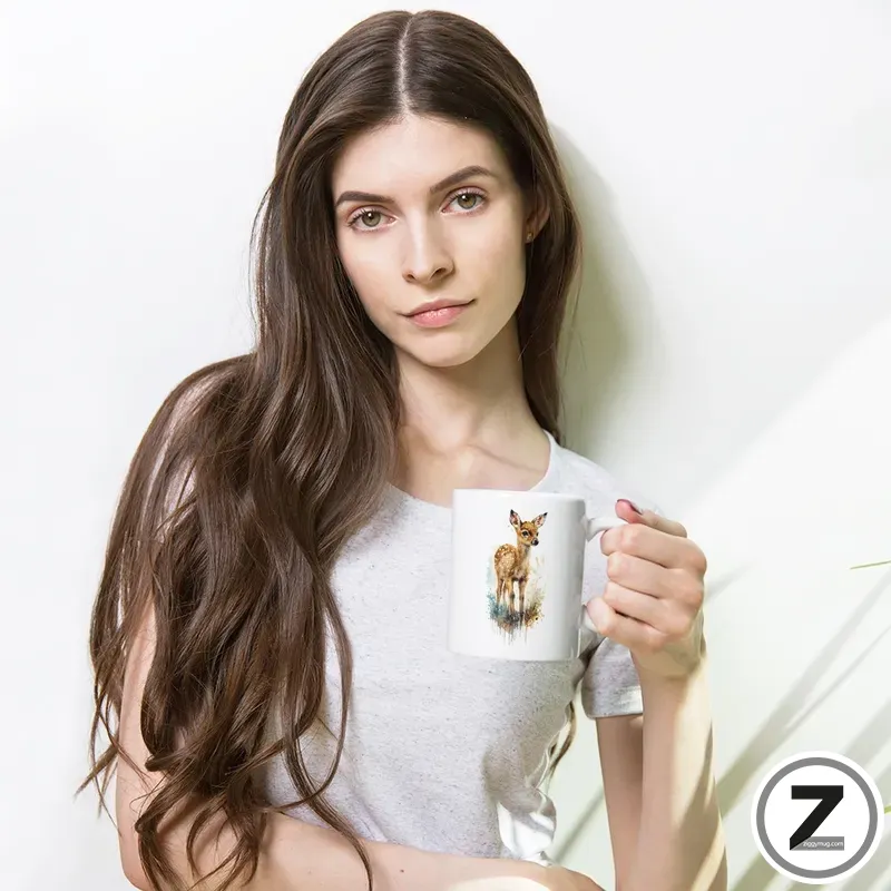 Young woman with long brown hair in a light gray shirt holds a white mug featuring a deer illustration, against a bright pale background.