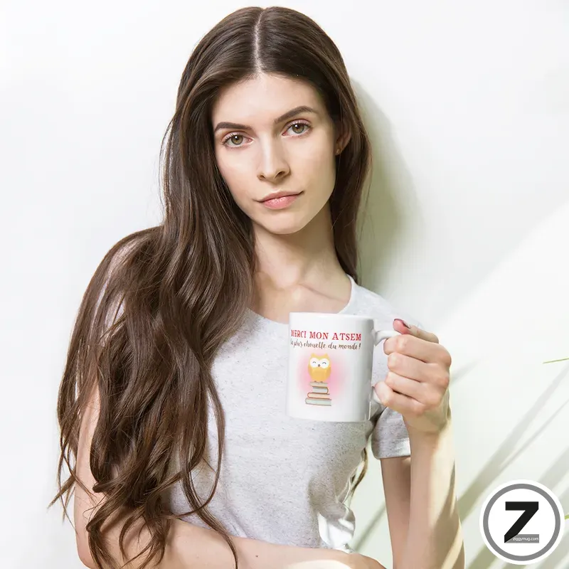 Woman with long brown hair holding a white mug with a small cartoon image on it, against a light background.