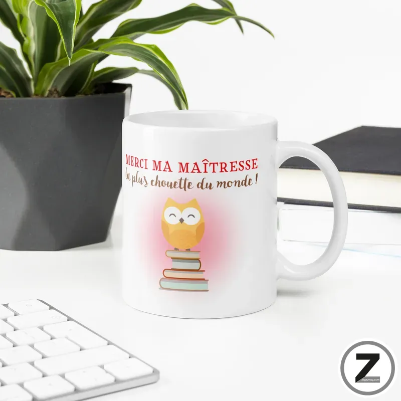 White mug with a design: a smiling orange owl sitting on a stack of books, with red French text above reading 'MERCI MAITRESSE' and a light pink glow behind the owl.