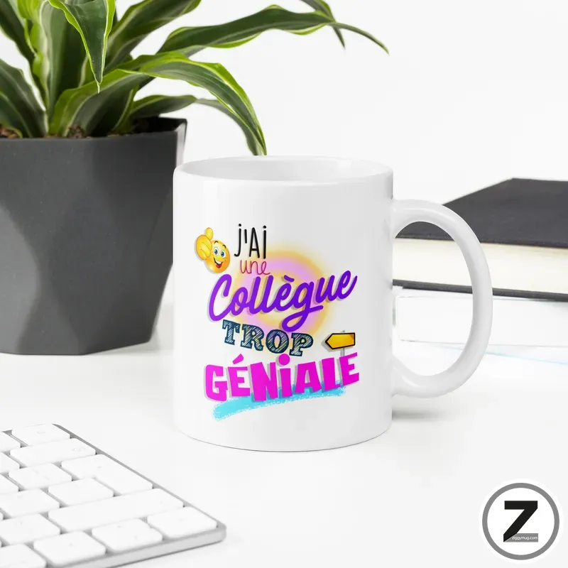 White ceramic mug with colorful text 'J'ai une collègue trop géniale' on a clean desk beside a plant and keyboard.