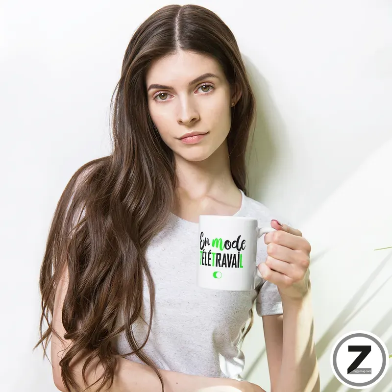 Woman with long brown hair in a light gray shirt, holding a white mug that reads 'En mode télétravail' against a white background.