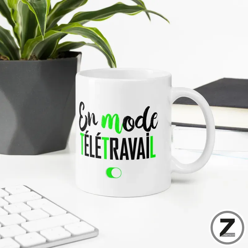 White ceramic mug on a clean desk with the phrase 'En mode Télétravail' in black and green lettering, plant in background and keyboard nearby.