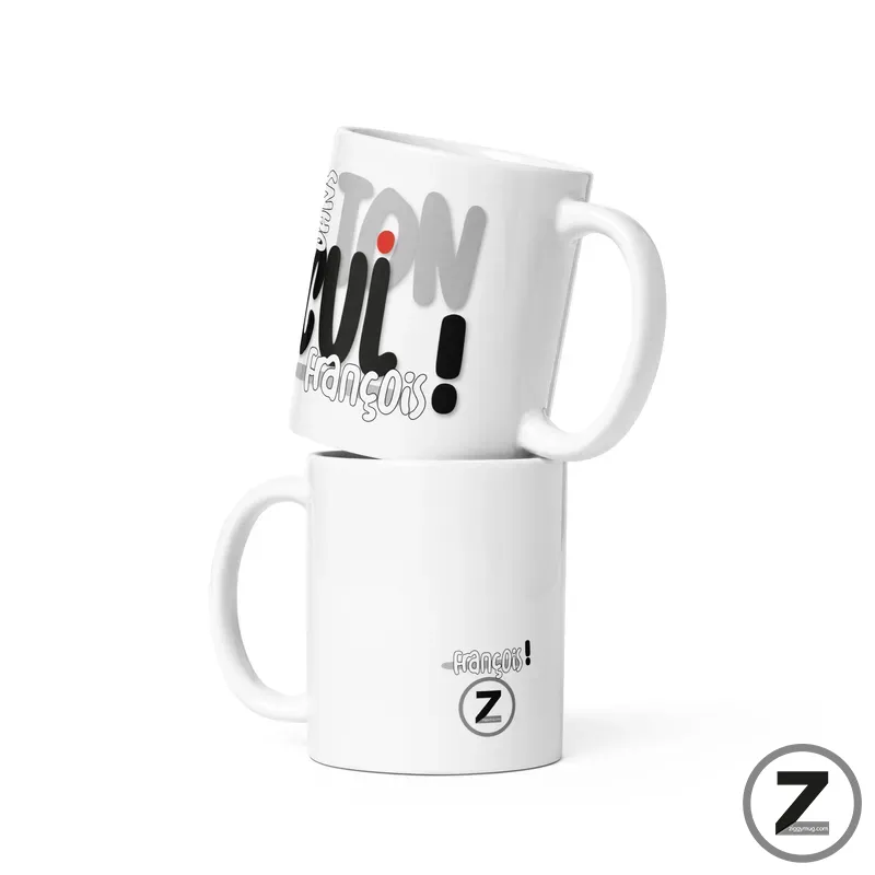 Two white ceramic mugs stacked, top mug tilted to show a graphic with black text and a red dot accent.