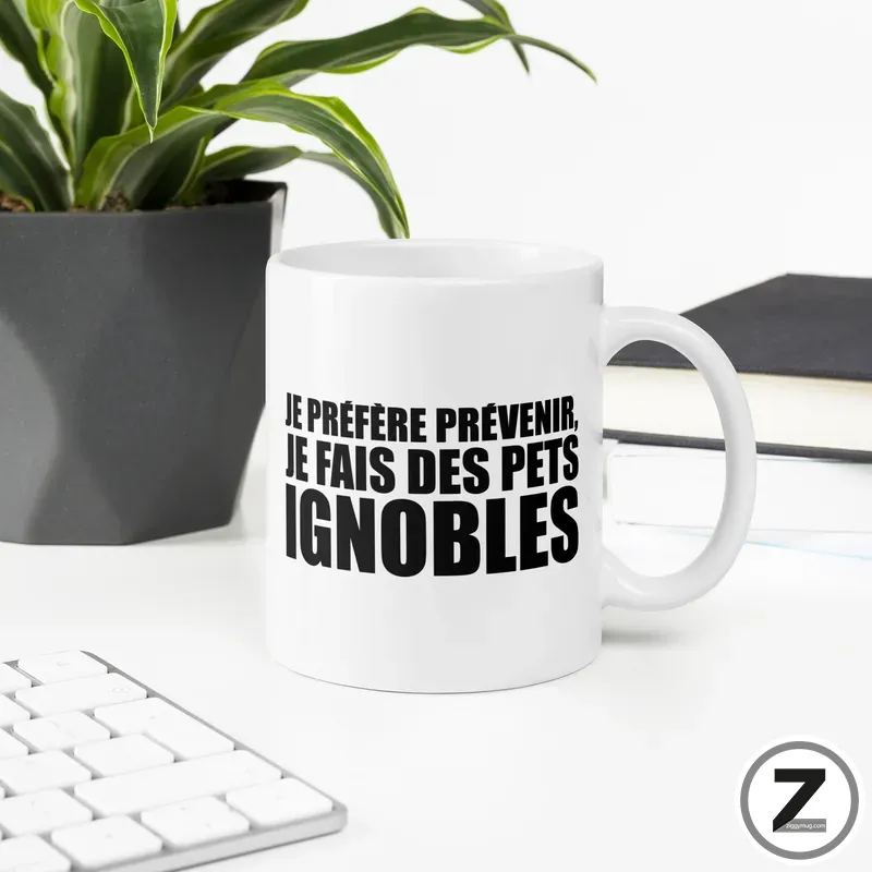 White ceramic mug on a desk with a bold black French slogan printed on it: 'Je préfère prévenir, je fais des pets ignobles'