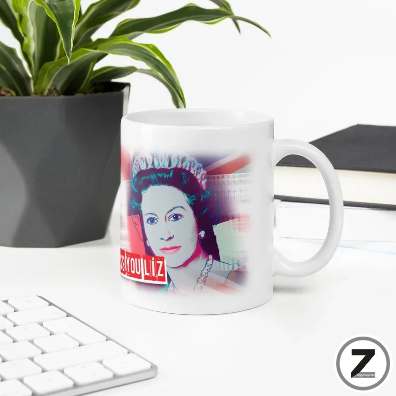 White mug on a desk featuring a colorful pop-art portrait of a woman with bold red text, with a plant and keyboard nearby.