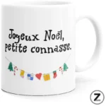 White mug featuring the handwritten French message 'Joyeux Noël, petite connasse.' above a small garland of colorful holiday icons (trees, stockings, hearts).
