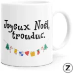 White ceramic mug with the French holiday message 'Joyeux Noel, trouduc.' in black, and a string of colorful festive decorations beneath.