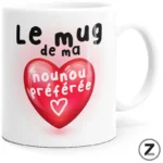 White ceramic mug featuring a pink heart graphic and the French text 'Le mug de ma nounou préférée' (my nanny's favorite mug).