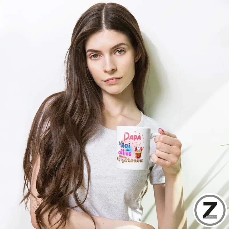 Young woman with long brown hair holding a white mug with colorful French text, standing against a light background.
