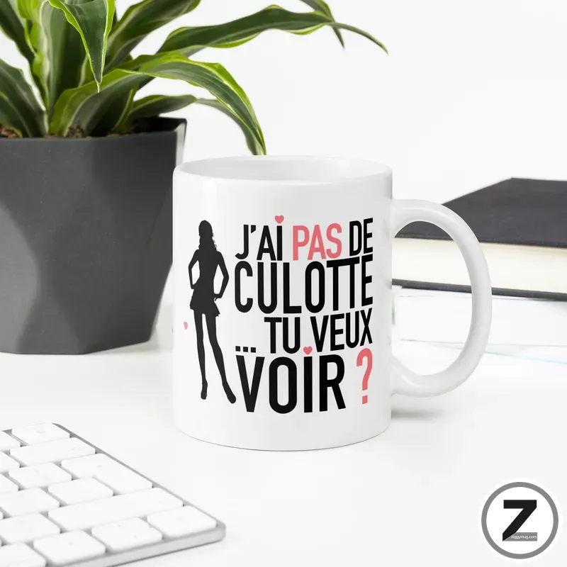 White mug with a black silhouette of a woman and bold French text 'J'ai pas de culotte tu veux voir ?' in red accents on a white desk.