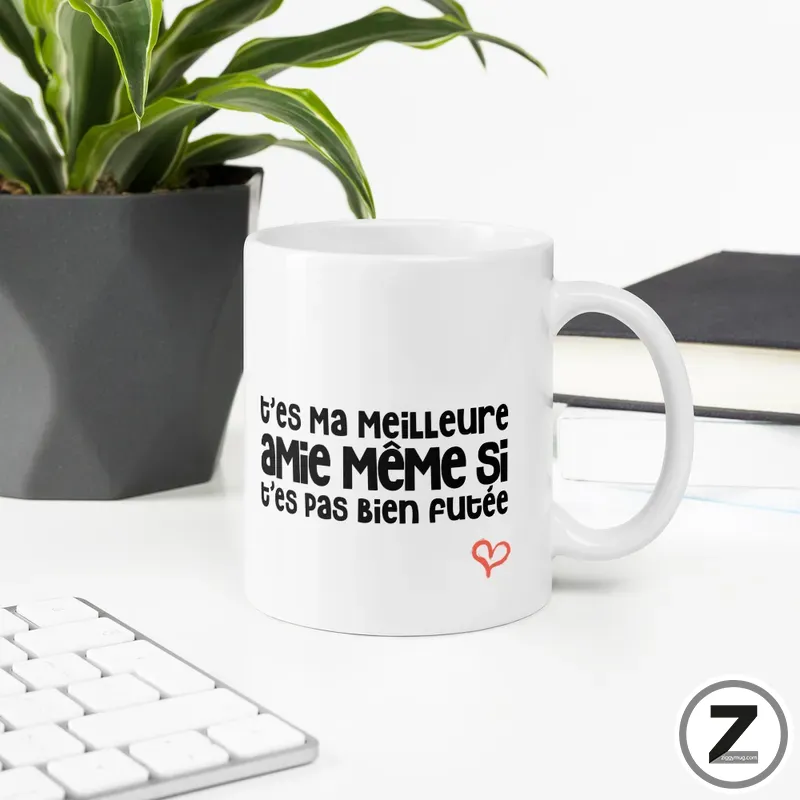 White ceramic mug on a desk with bold French text and a small red heart, near a plant and keyboard.