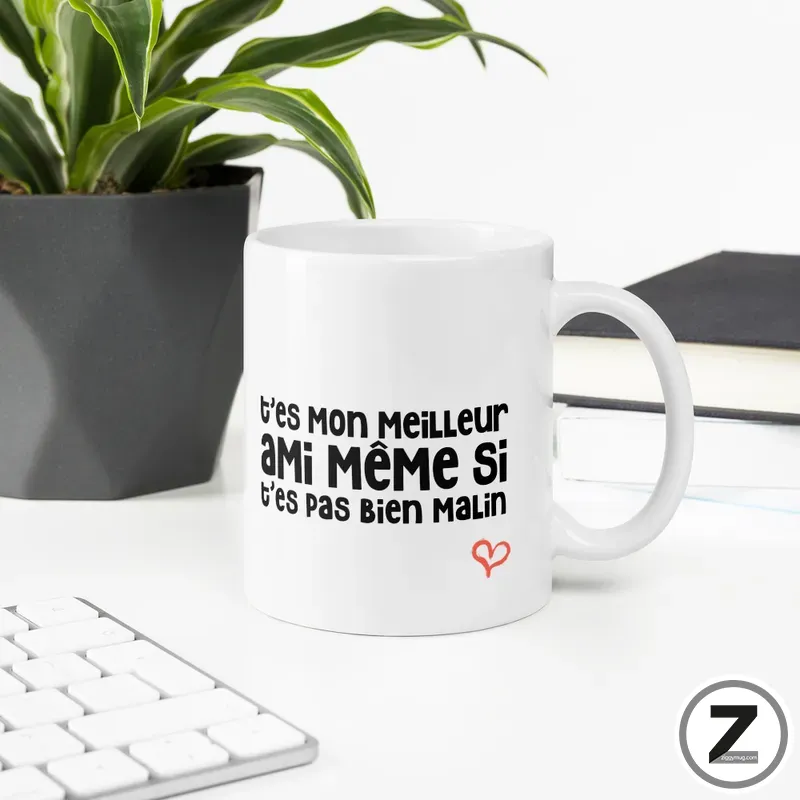 White ceramic mug on a desk, printed with a French joke phrase and a small red heart: 't'es mon meilleur ami même si t'es pas bien malin'.