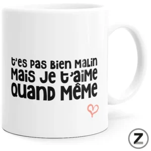 White mug with bold French phrase 't'es pas bien malin mais je t'aime quand même' and a small pink heart ornament.