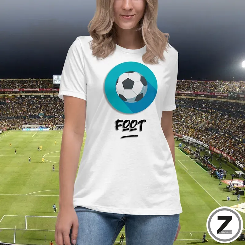 Woman wearing a white T-shirt with a teal circular soccer-ball logo and the word FOOT, standing in a stadium background.